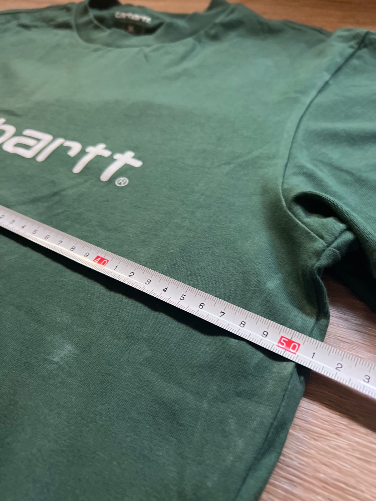 A tape measure measuring the width of the green Carhartt T-shirt
