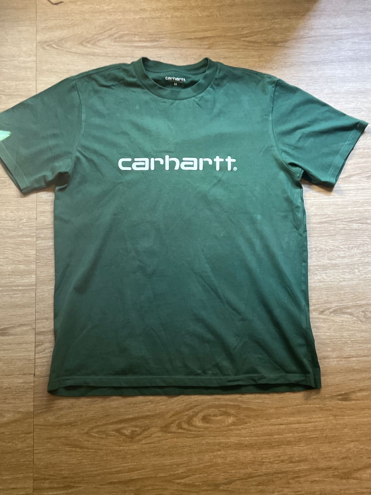The phone photo: a green Carhartt T-shirt on the wooden floor at home