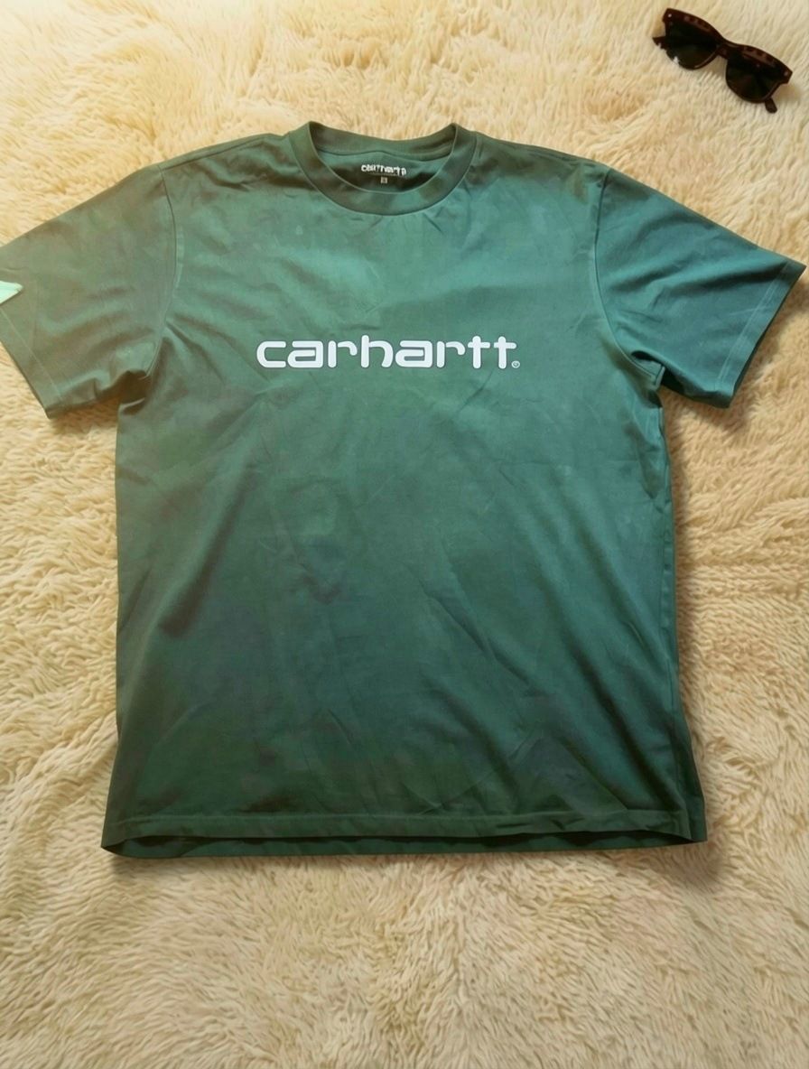 The same green Carhartt T-shirt on a light studio rug